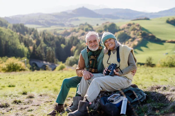 秋の自然の中でハイキング中に座って休憩を取っているシニアカップル — ストック写真