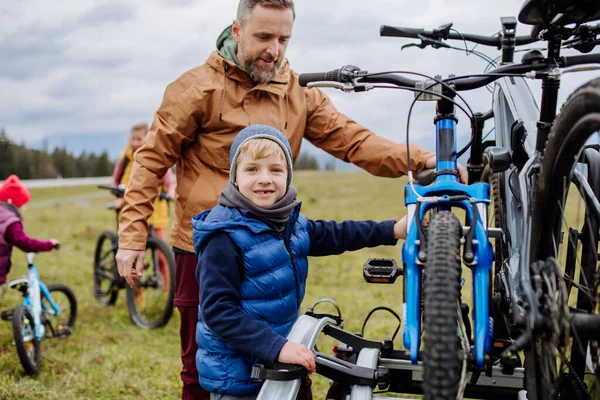 自然の中で自転車に乗る準備をしている小さな子供を持つ若い家族は 車のラックから自転車を置きます 健康的なライフスタイルと移動活動の概念 — ストック写真