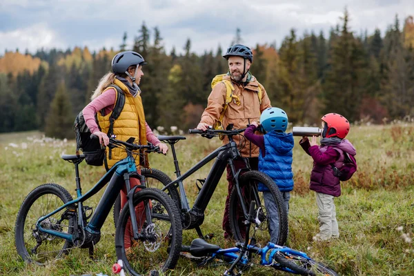 Young family with little children preparing for bicycle ride in nature, putting off bicycles from car racks. Concept of healthy lifestyle and moving activity.