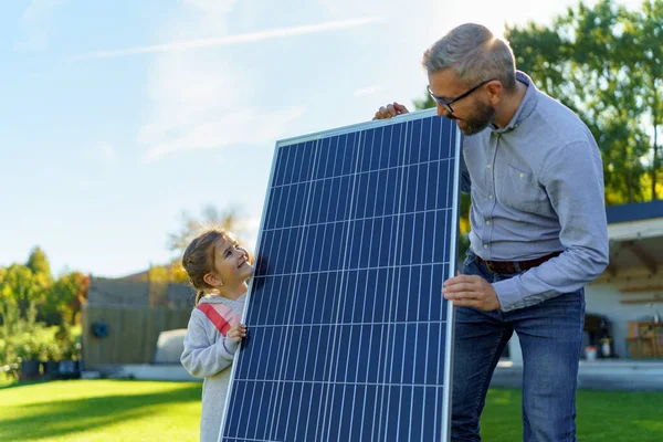 父亲和他的小女儿在房子附近用太阳能电池板 替代能源 节约资源和可持续生活方式概念 — 图库照片