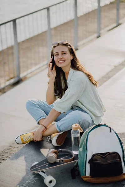 幸せな若い女性はスケートボードに座って街の橋を呼び出します 若者文化と通勤概念 — ストック写真