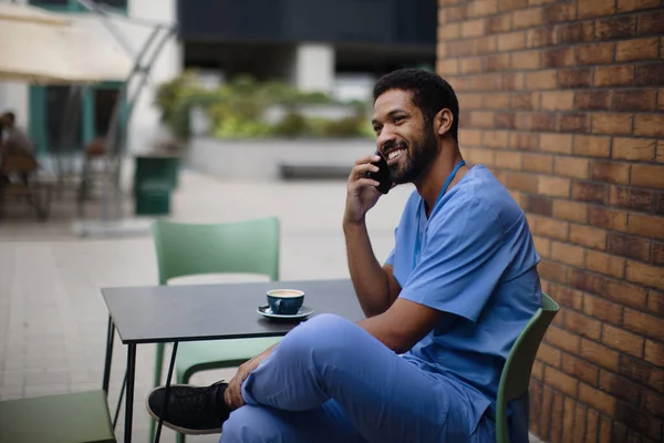 Nurse man calling and sitting, outdoor at a cafe.