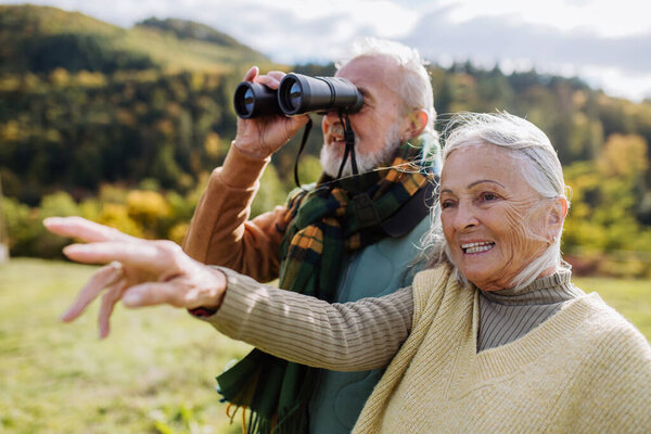 Senior couple looking at view trough a binoculars on autumn walk.
