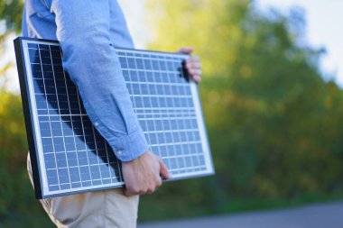 Mid section of businessman holding solar panel, standing outdoor at a garden. clipart