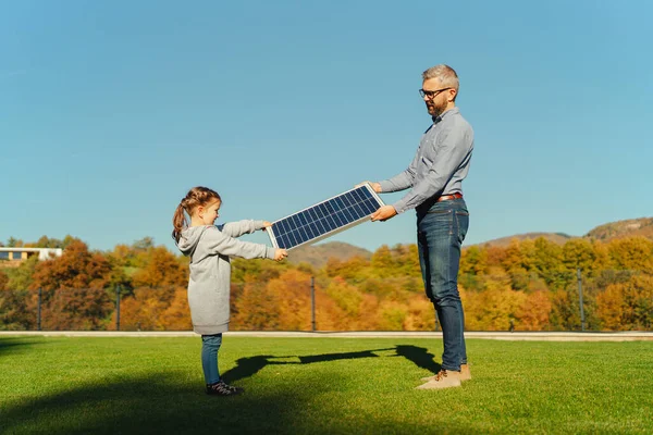 父亲和他的小女儿在太阳能电池板上晒太阳 在后院充电 替代能源 节约资源和可持续生活方式概念 — 图库照片