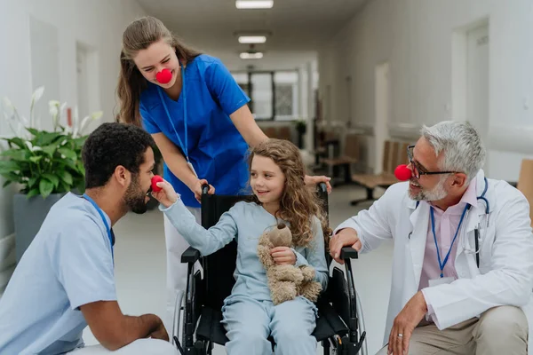 stock image Happy doctors with a clown red noses taking care about little girl.