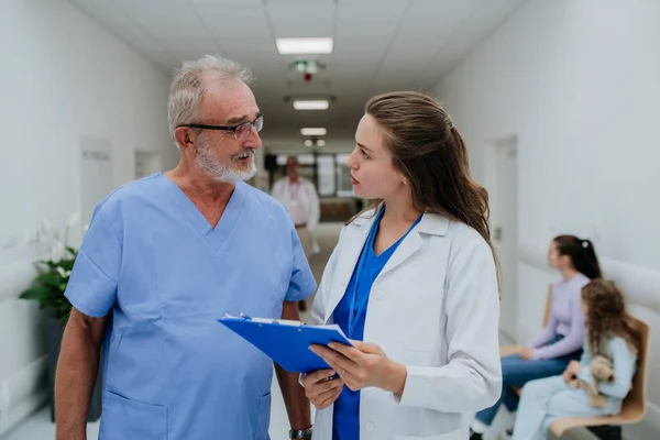 高齢の医師は彼の若い同僚に助言を与え 病院の廊下で議論する ヘルスケアの概念 — ストック写真