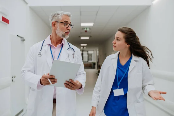 高齢の医師は彼の若い同僚に助言を与え 病院の廊下で議論する ヘルスケアの概念 — ストック写真