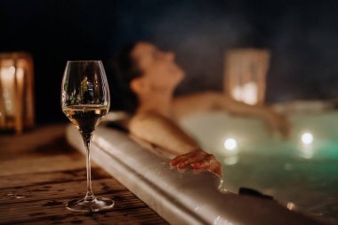 Genç bir kadın soğuk bir kış akşamında terasında bir bardak şarapla dışarıda küvetin keyfini çıkarıyor..