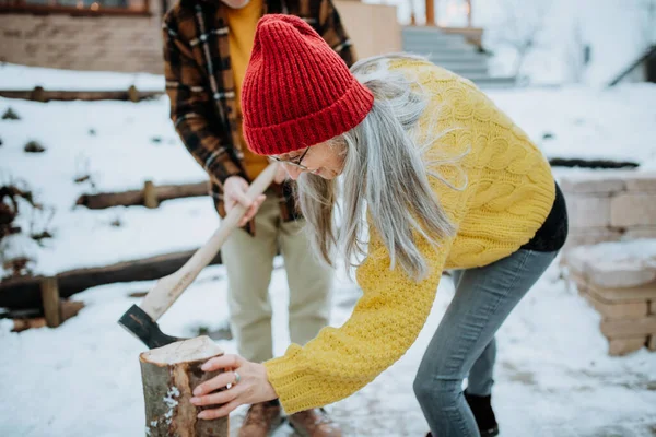寒い冬の日の間に 彼らの家の前で一緒に木を切るシニアカップル — ストック写真
