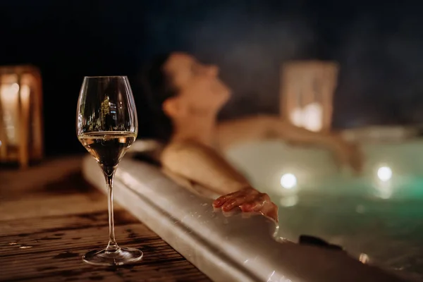 在寒冷的冬夜 年轻女子在阳台边喝一杯葡萄酒 享受户外浴缸 — 图库照片