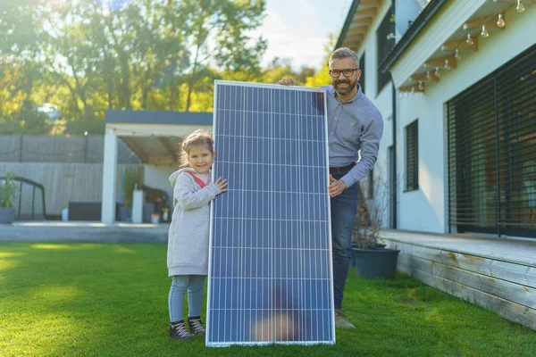 Ojciec Swoją Córeczką Łapie Słońce Panelu Słonecznym Szarżuje Podwórku Alternatywna — Zdjęcie stockowe