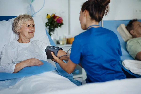 Молодая Медсестра Измеряет Давление Крови Пожилого Пациента — стоковое фото