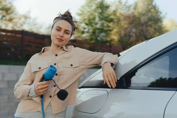 Arabasından Elektrik Kablosu Tutan Genç Bir Kadın Onu Evde Şarj — Stok fotoğraf