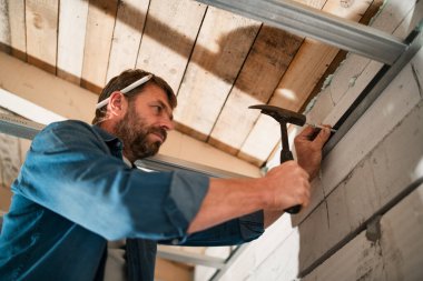 Olgun bir tamirci bitmemiş bir evde çivi çakıyor..