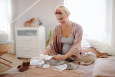 Mutlu hamile kadın, bebek kıyafetlerine bakıyor..
