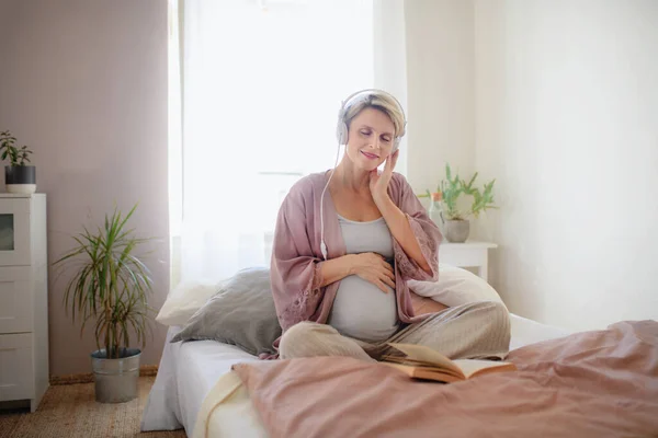 Έγκυος Γυναίκα Κάθεται Ένα Κρεβάτι Ακούγοντας Μουσική Και Διαβάζοντας Βιβλίο — Φωτογραφία Αρχείου