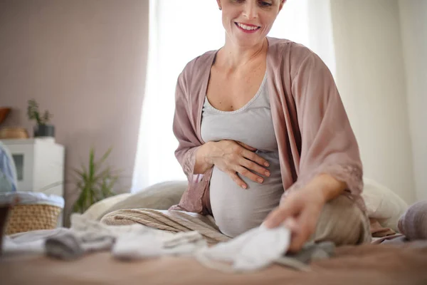 Mujer Embarazada Feliz Mirando Poca Ropa Bebé —  Fotos de Stock