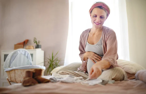 Szczęśliwa Kobieta Ciąży Patrząc Małe Ubrania Dziecka — Zdjęcie stockowe