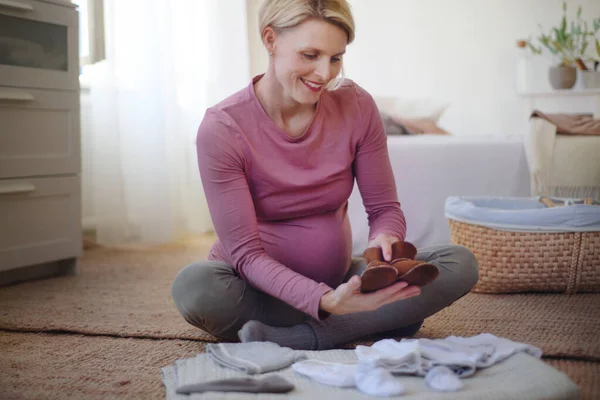 Szczęśliwa Kobieta Ciąży Patrząc Małe Ubrania Dziecka — Zdjęcie stockowe