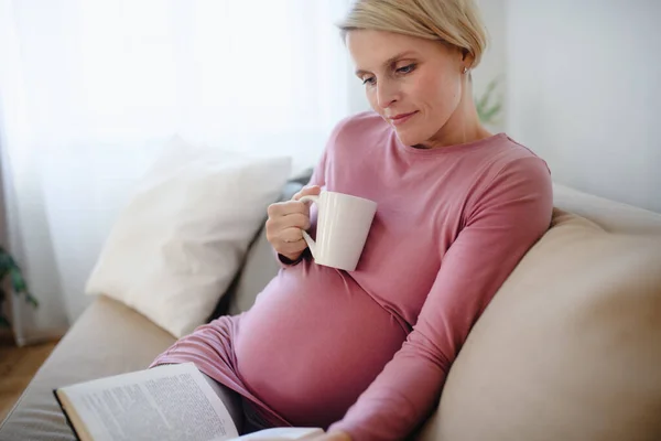 Έγκυος Γυναίκα Κάθεται Στον Καναπέ Διαβάζοντας Βιβλίο Και Απολαμβάνοντας Ένα — Φωτογραφία Αρχείου