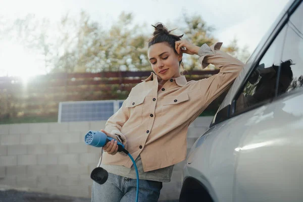 Arabasından Elektrik Kablosu Tutan Genç Bir Kadın Onu Evde Şarj — Stok fotoğraf