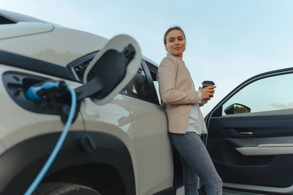 Mladá Žena Šálkem Kávy Čeká Zatímco Nabíjení Elektrických Automobilů Udržitelný — Stock fotografie