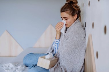 Sick woman sitting in a bed, having a cold. clipart