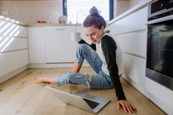 年轻女人坐在厨房里 手里拿着笔记本电脑和咖啡 — 图库照片