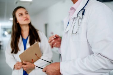 Yaşlı doktor genç meslektaşına tavsiye veriyor, hastane koridorunda tartışıyor. Sağlık hizmeti kavramı.