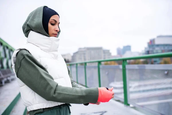 Young muslim woman putting on sports gloves, outdoor in a city street.