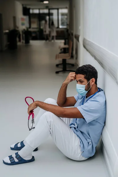 忧心忡忡的年轻医生坐在医院走廊地板上 — 图库照片