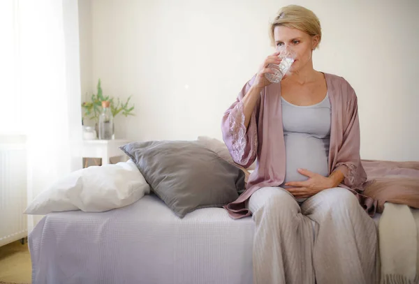 Pregnant woman drinking water in a bed, at morning. Healthy lifestyle and morning routine in pregnancy, concpet.
