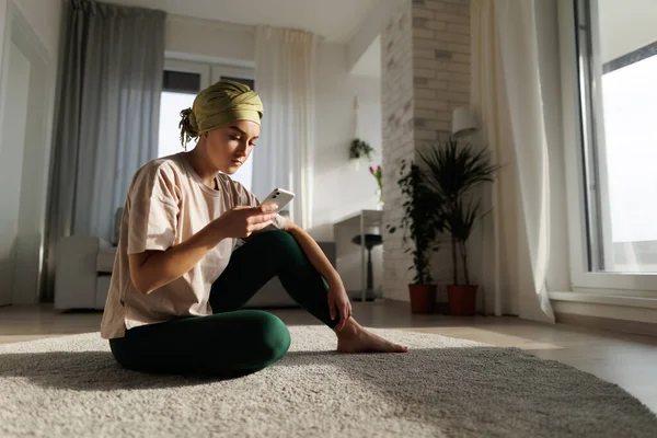Young woman with cancer siting at home and scrolling a phone.
