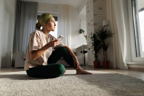 Young woman with cancer siting at home and scrolling a phone.