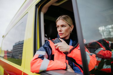 Portrait of a young woman doctor sitting and talking in to walkie-talkie in ambulance car.