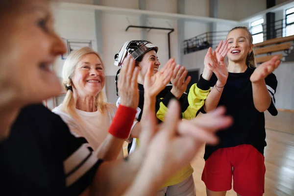 A group of young and old cheerful women, floorball team players, in gym cebrating victory.