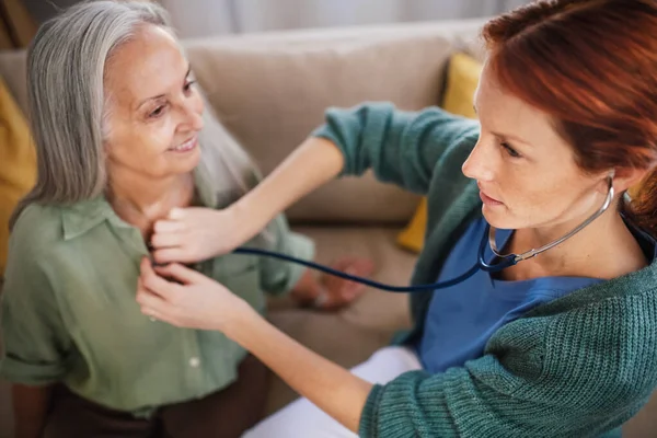 Nurse examining senior patient with stethoscope at home.