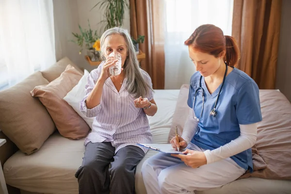 stock image Nurse cosulting with senior woman her health condition and taking pills, at her home.