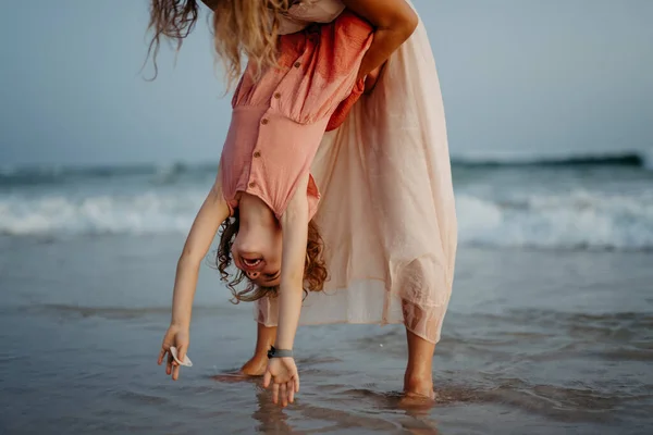 Mother holding her daughter upside down, enjoying summer vacation and having fun.