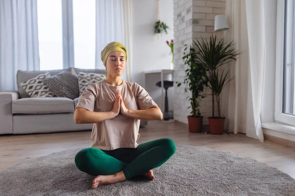 Young woman with cancer taking yoga and meditating in the apartment.