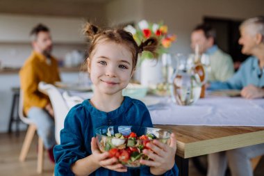 Little girl holding bowl with salad, preparations for a family dinner.