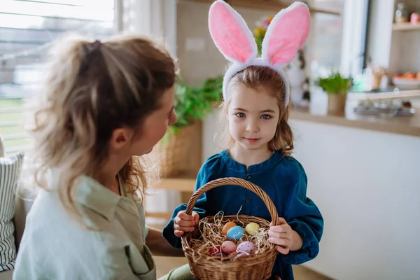 Little girl with bunny ears holding basket and showing mother easter eggs which she found.