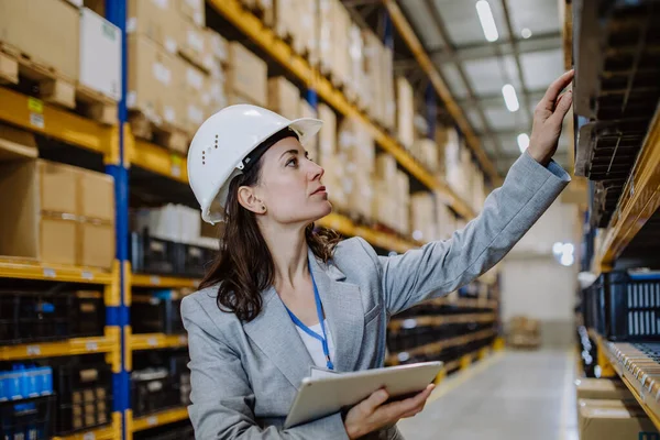 Manager woman in suit controlling goods in warehouse.