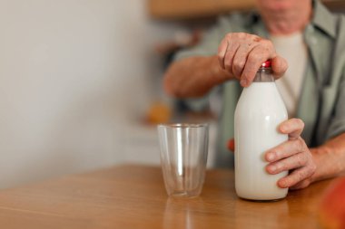 Close up of senior man sitting in kitchen and pouring milk in a glass. Healthy lifestyle concept.