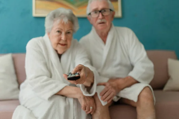 Happy Senior Couple Sitting Sofa Bathrobes Watching — Stok fotoğraf