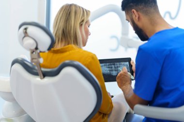 Dijital tablette hastaya röntgen taraması gösteren dişçinin arka görünümü.