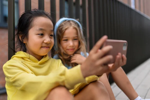 Kapüşonlu Küçük Kızlar Kaldırımda Oturuyor Akıllı Telefon Çeviriyor — Stok fotoğraf
