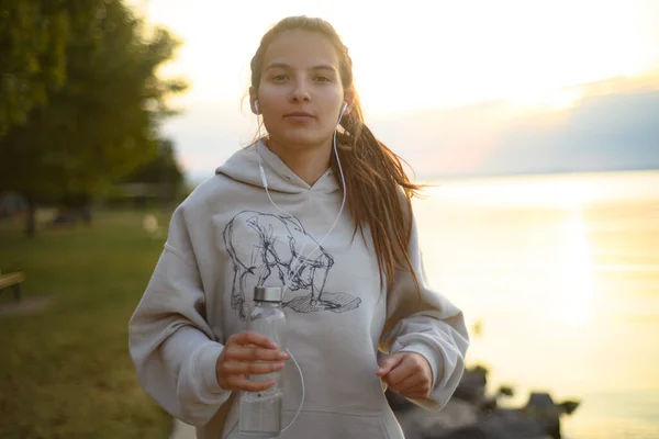 Молодая Красивая Спортивная Девушка Слушает Музыку Восходе Солнца Озера — стоковое фото