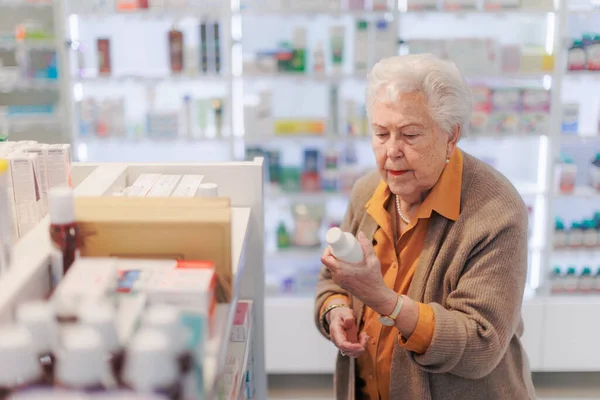 老年妇女站在药店 阅读药箱上的文字 — 图库照片